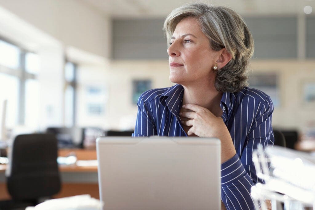 mature woman on laptop thinking and looking out window A52j1i