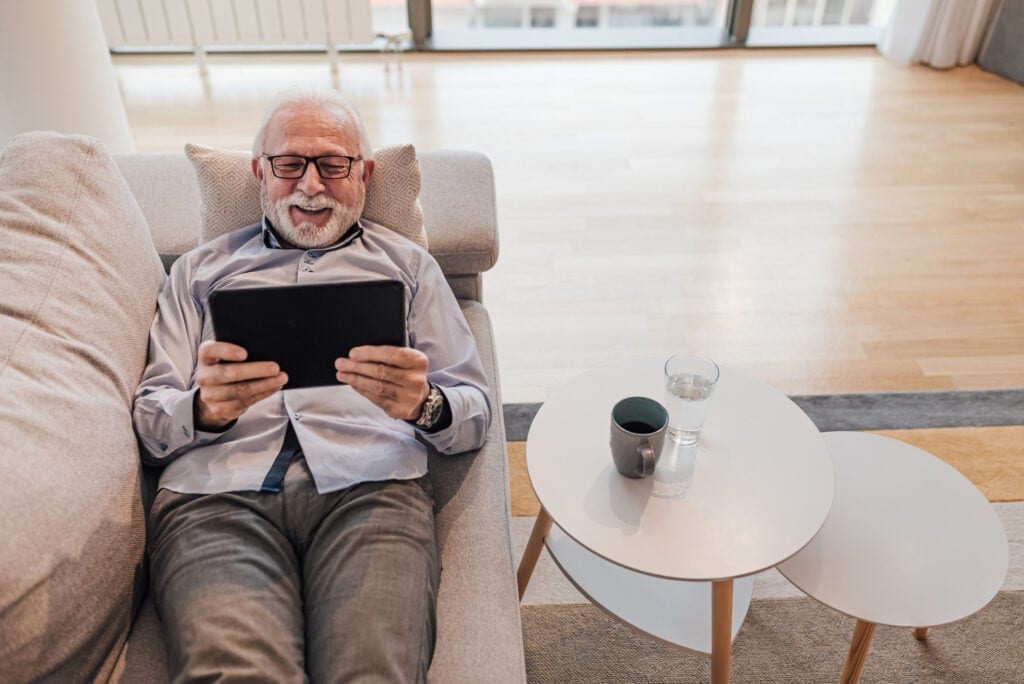 older man lying down on couch holding tablet gettyimages