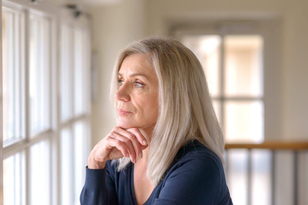 older person with serious expression looking out a window KZdjA
