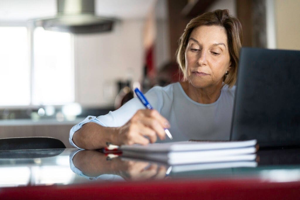 older woman taking notes laptop gettyimages