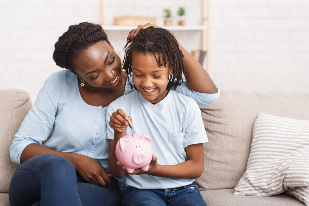 parent and child putting coins into piggy bank at home