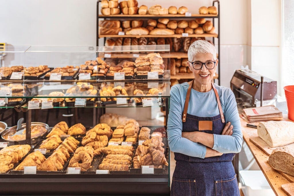 senior woman working a smiling person wearing an apron in a bakery gettyimages JdRWf