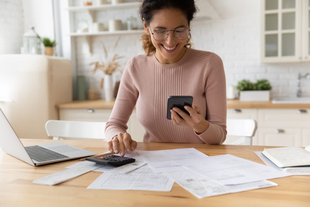 smiling person looking at smartphone and typing on calculator