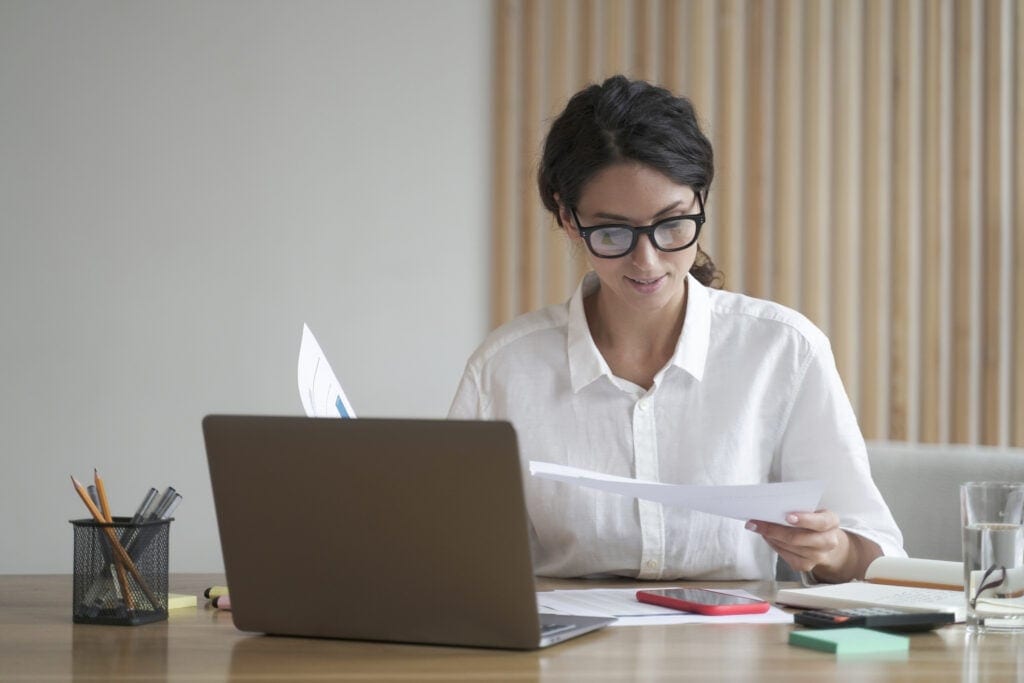 a person sitting at a desk reviewing documents in front of a computer monitor