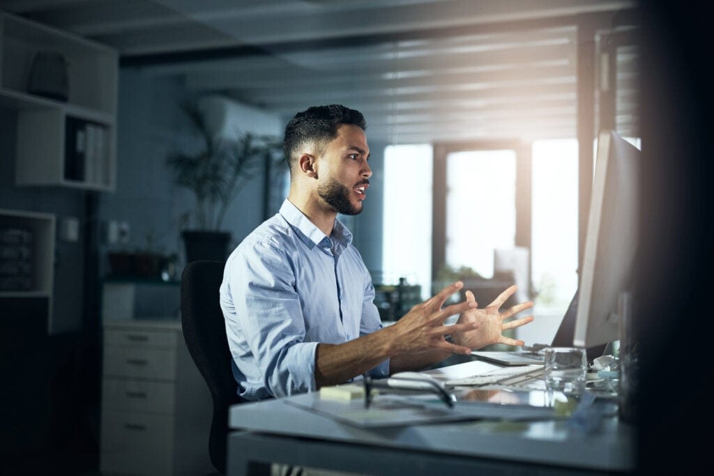 an angry person with hands outstretched looking at a computer monitor