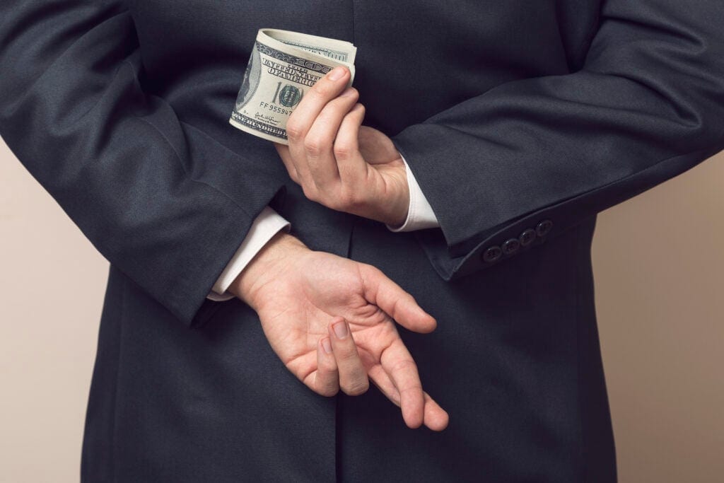 businessman holding cash money bills behind back fingers crossed embezzle getty