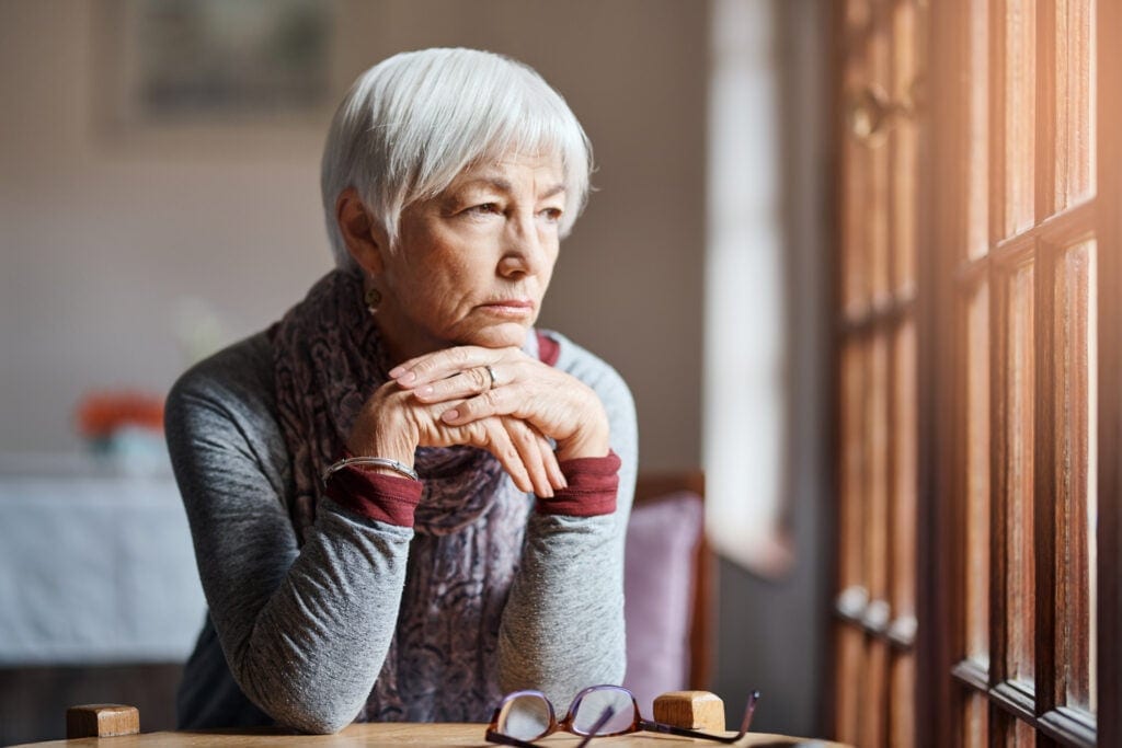 older person sitting at a table looking out a window