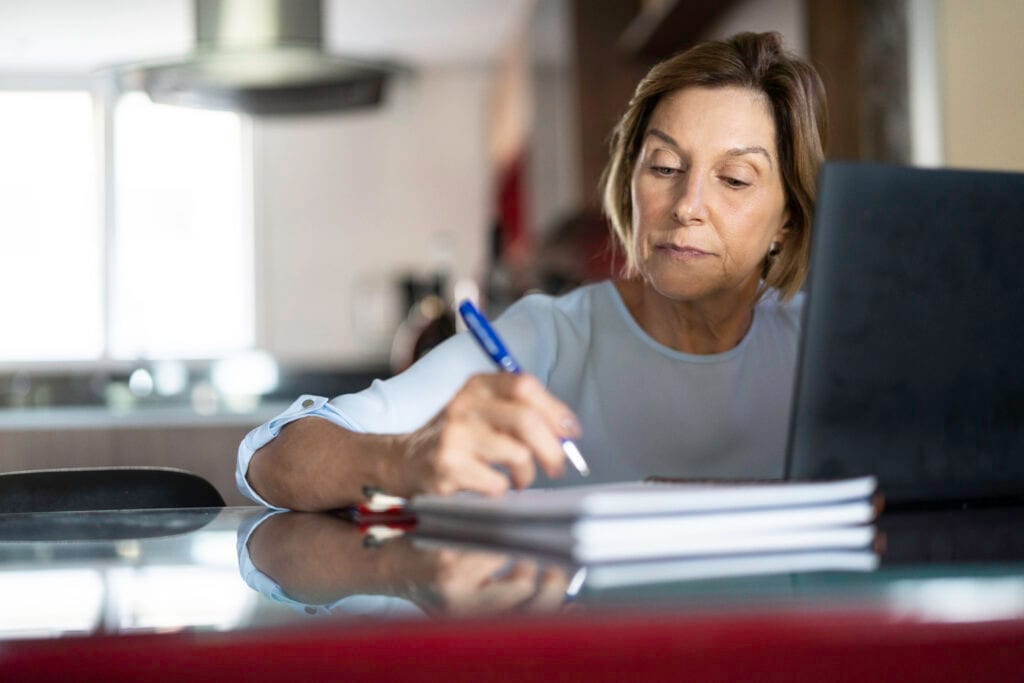 older woman taking notes laptop gettyimages