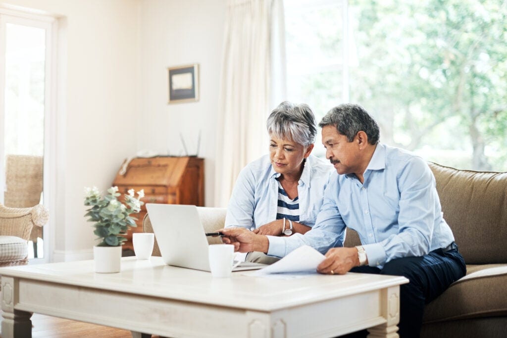 two older people sitting on a couch looking at a laptop copy
