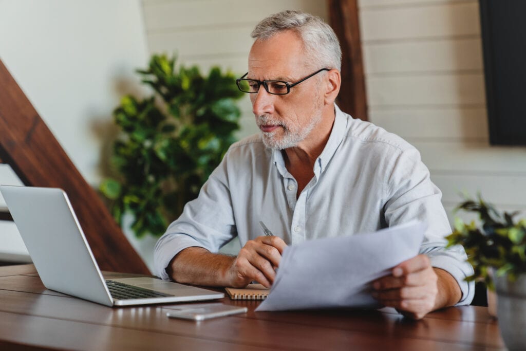 older man laptop holding papers gettyimages