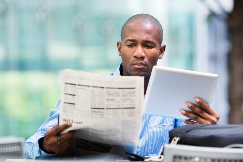 Man reading newspaper and looking at a tablet.width dtWRvy.jpg