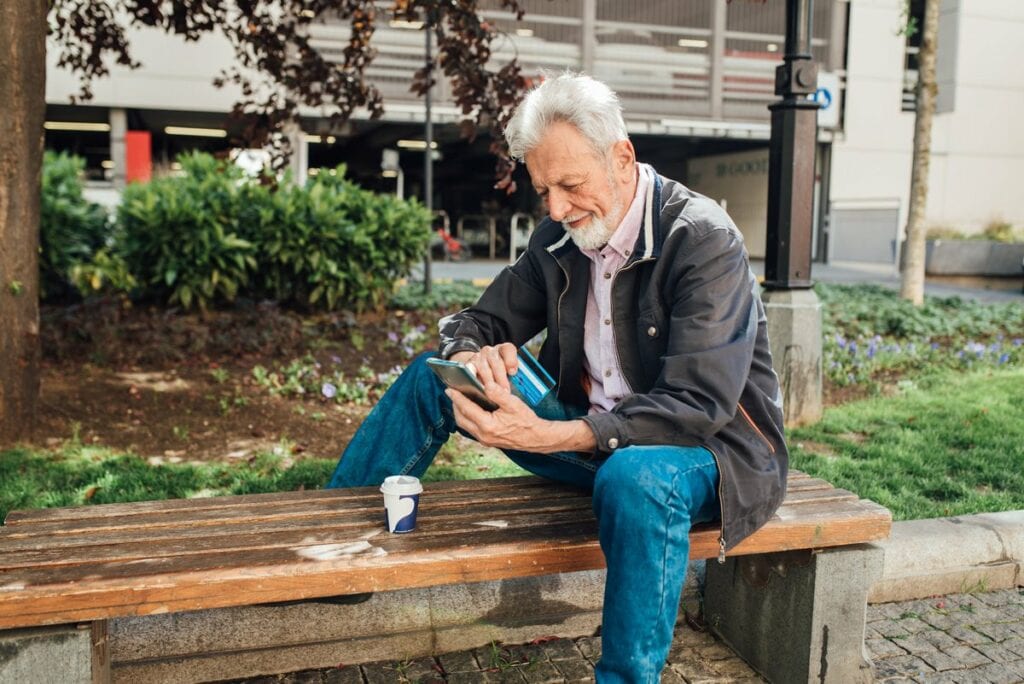 Older gentleman sitting on park bench using h.width Kwa