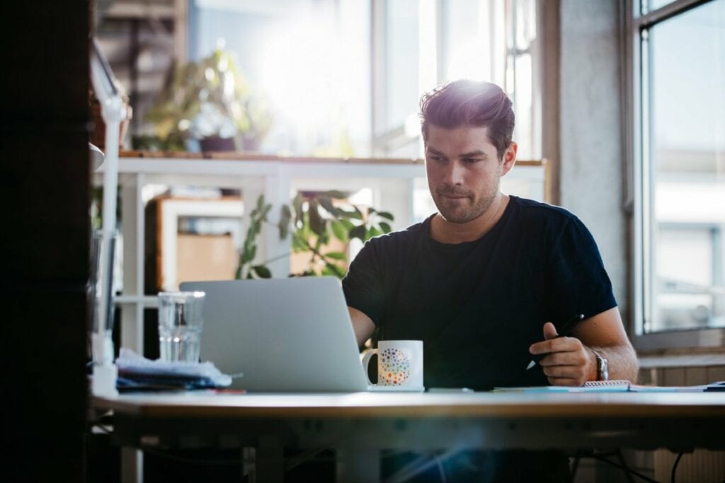 young man sitting at desk using laptop and th.width RMgeB