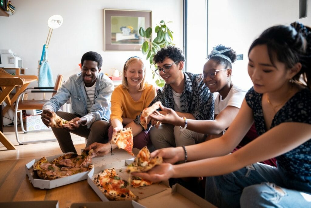 a group of friends eating pizza on an apartme.width DOHqAJ.jpg
