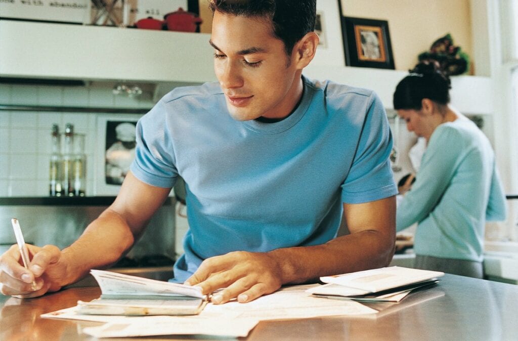 young man sitting at kitchen table writing a .width rpvXbE.jpg