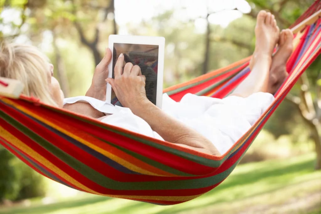senior woman relaxing in hammock reading ebook.jpg