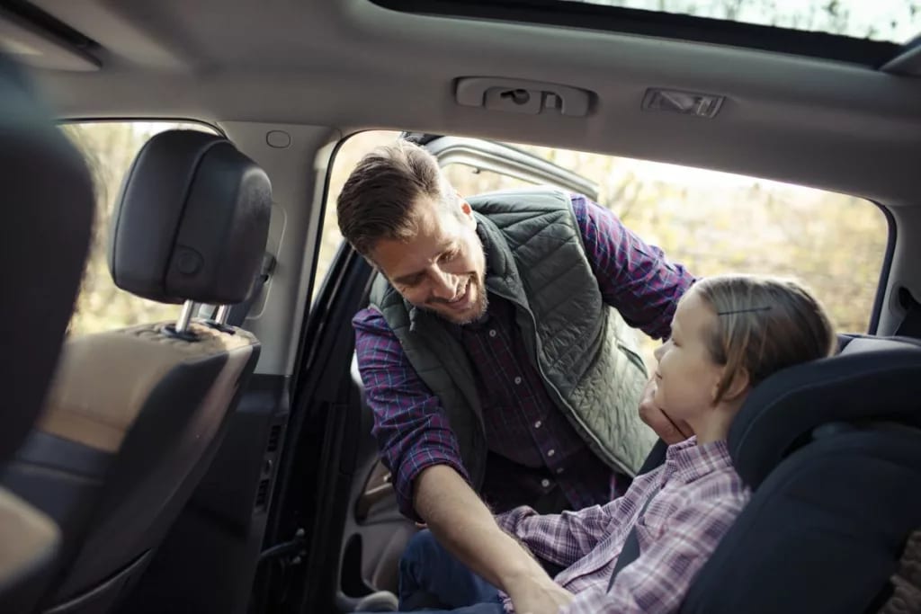 dad helping young daughter into car seat DYLl.width .jpg
