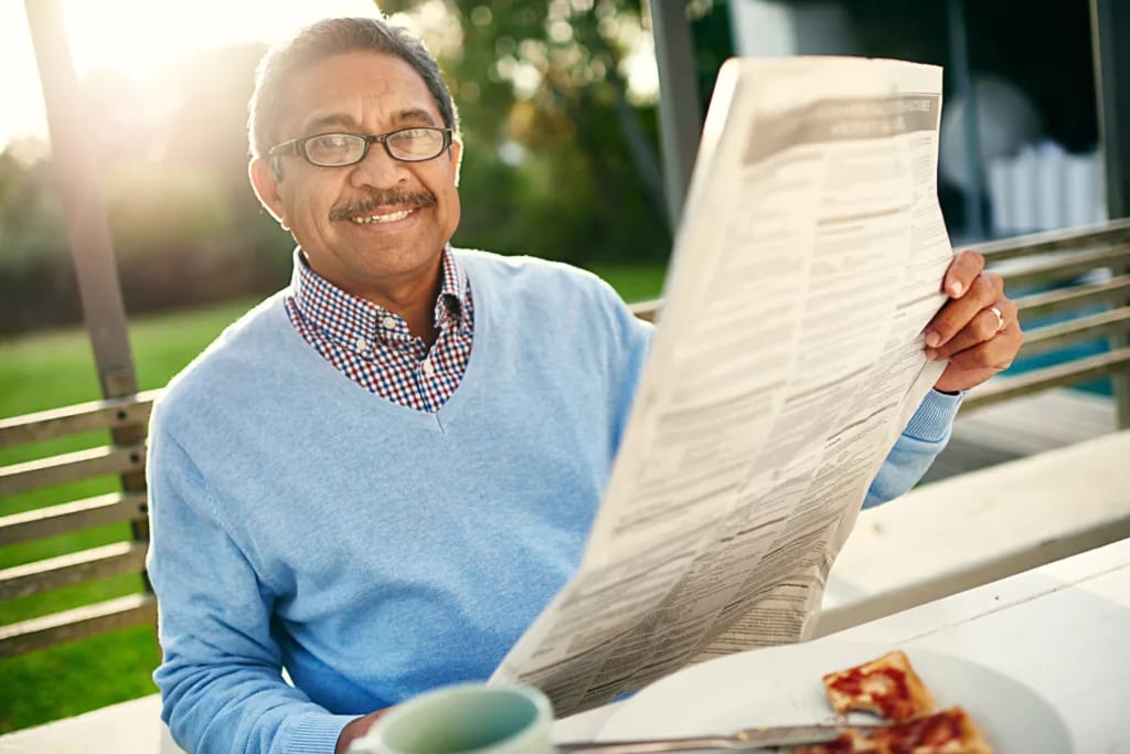 getty smiling person reading newspaper on bench outside.jpg