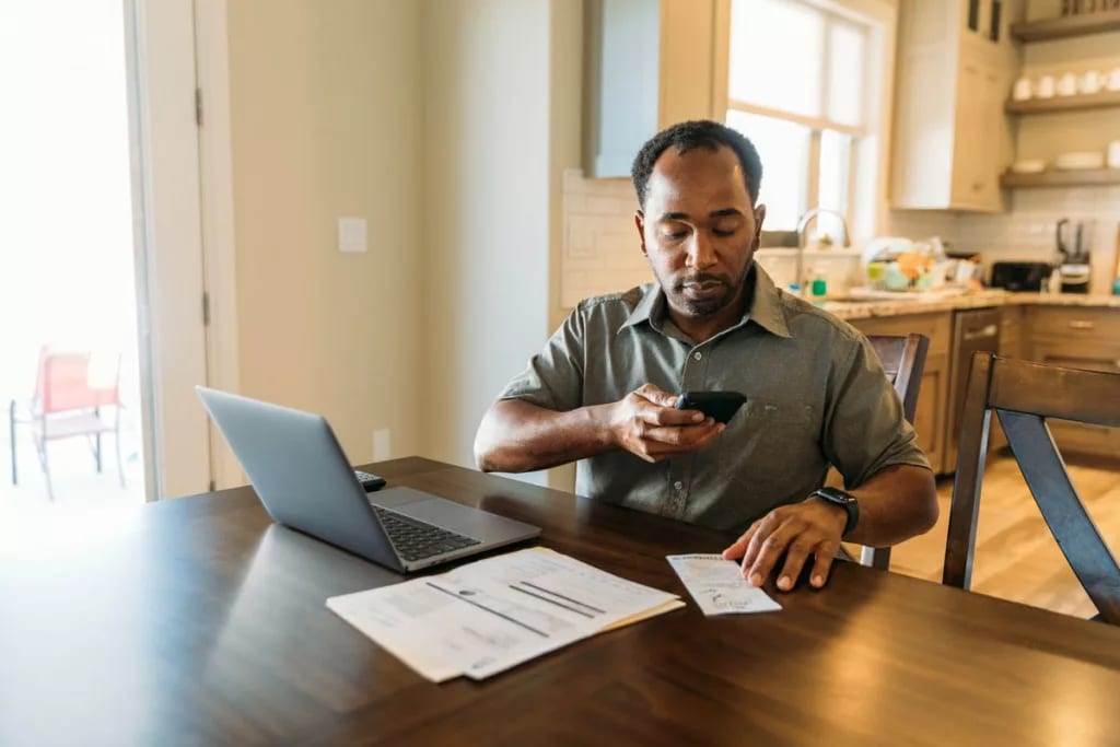 Man sits at counter with phone on laptop util.width QUam.jpg