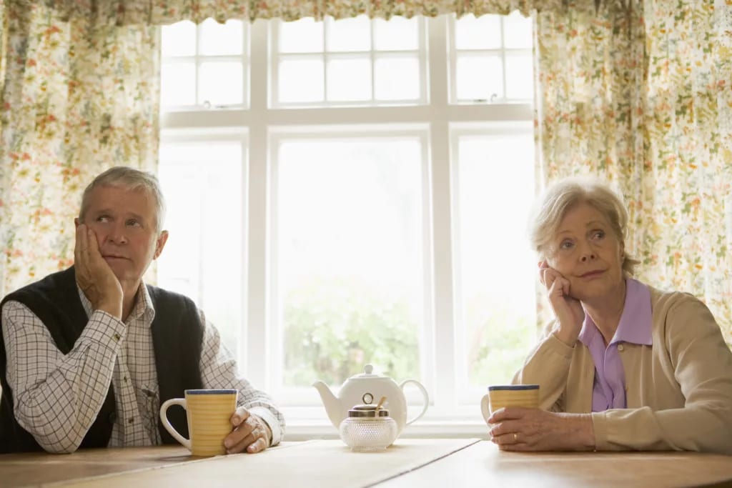 senior man and woman sitting at table resting their faces on their hands looking bored couple retirement.jpg