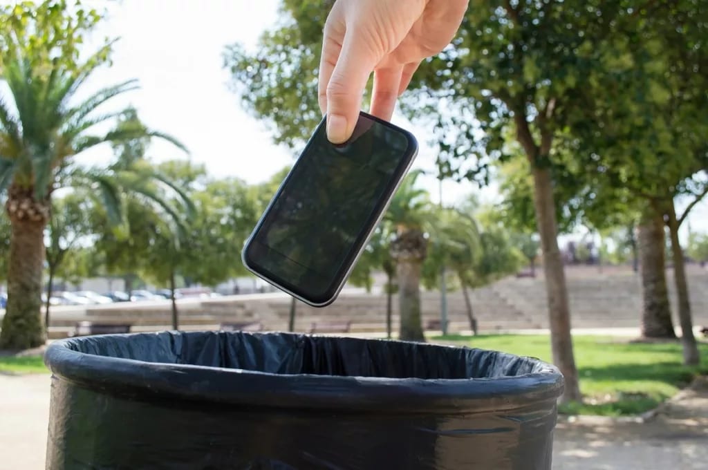 Hand dropping a smartphone into a waste baske.width .jpg