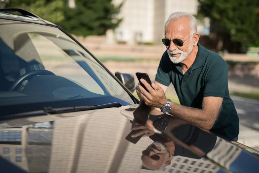 Mature man leans on car looking at phone LCHl.width .jpg