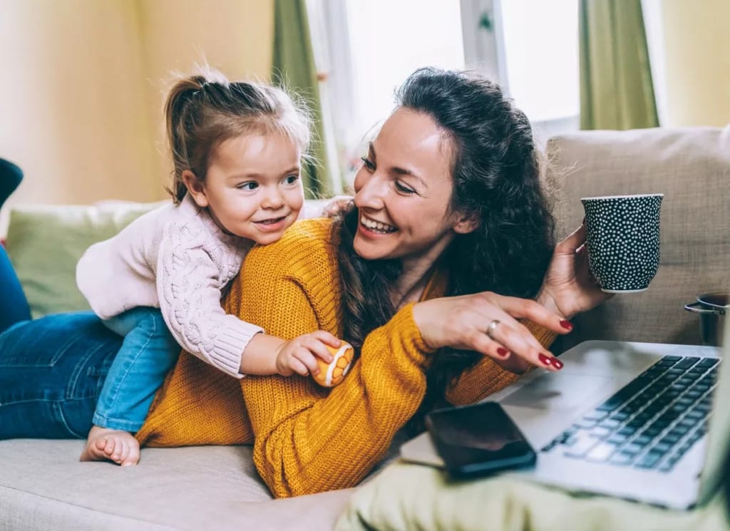 mom on computer with daughter climbing on her.width OikmpJ.jpg