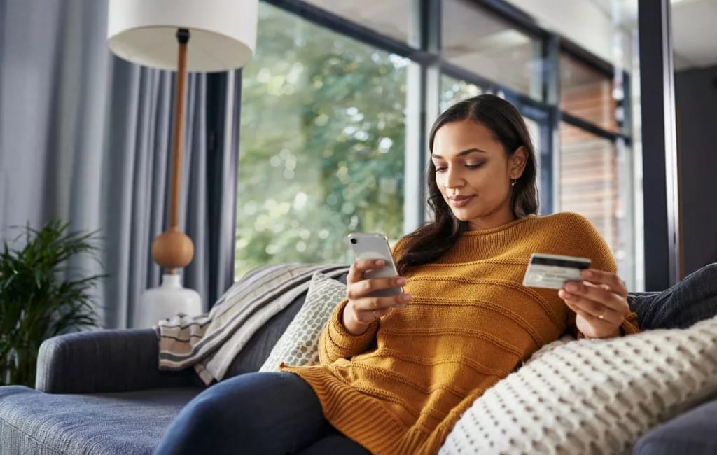Woman on couch holding phone and credit card .width cWRJtw.jpg