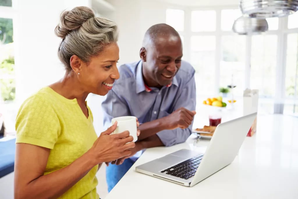 mature man and woman sitting in kitchen looking at laptop computer and smiling couple poc.jpg