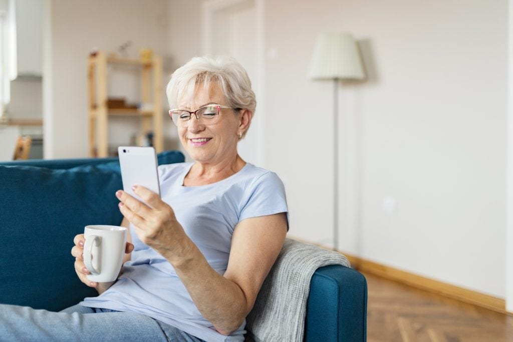 smiling senior holding coffee mug and looking at smartphone.jpg