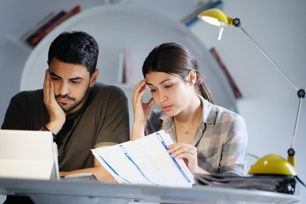 A young couple sadly looking through bills.