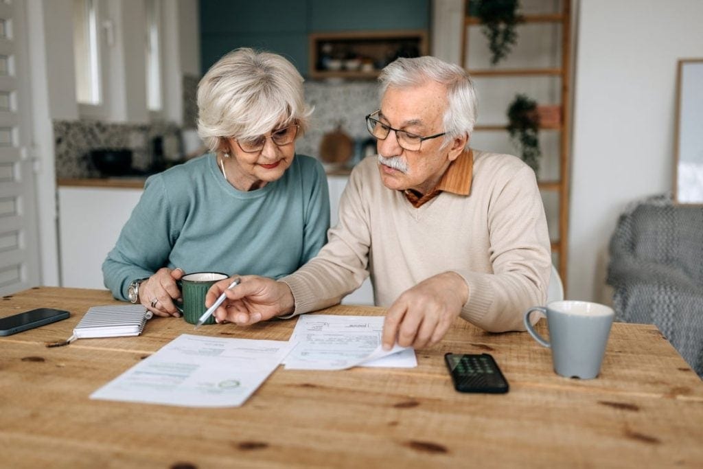 Older couple sitting at their kitchen table, reviewing their monthly budget.