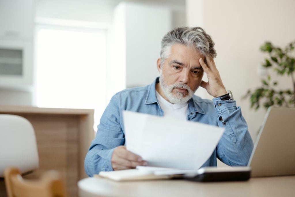 A person at a laptop holding a document.