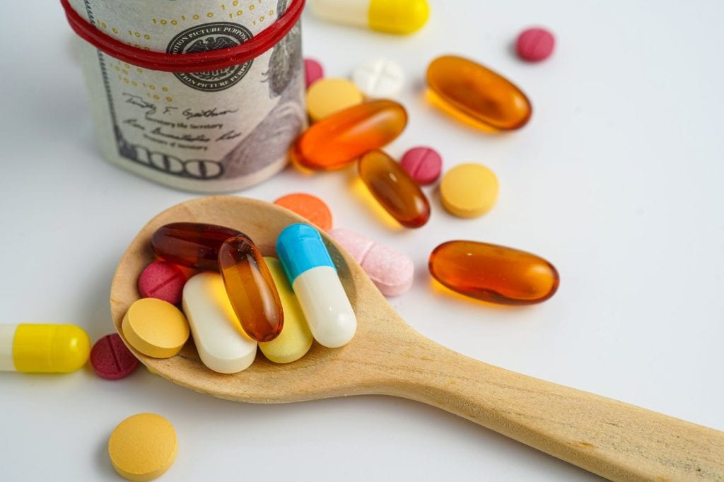 A wooden spoon with pills in it and a money roll in the background.