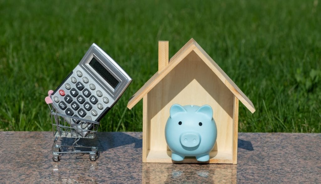 A piggy bank in a wooden house with a calculator next to it.