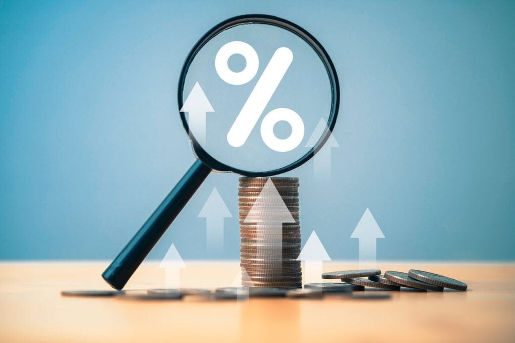A magnifying glass highlighting a percent sign on top of a coin stack.