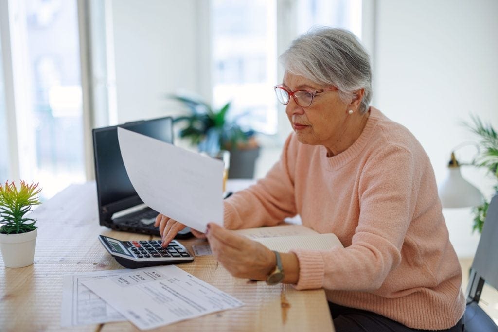 An older investor is using a calculator while reviewing a printed document.