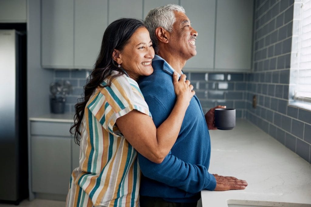 Older couple smiling as they look at their kitchen window.