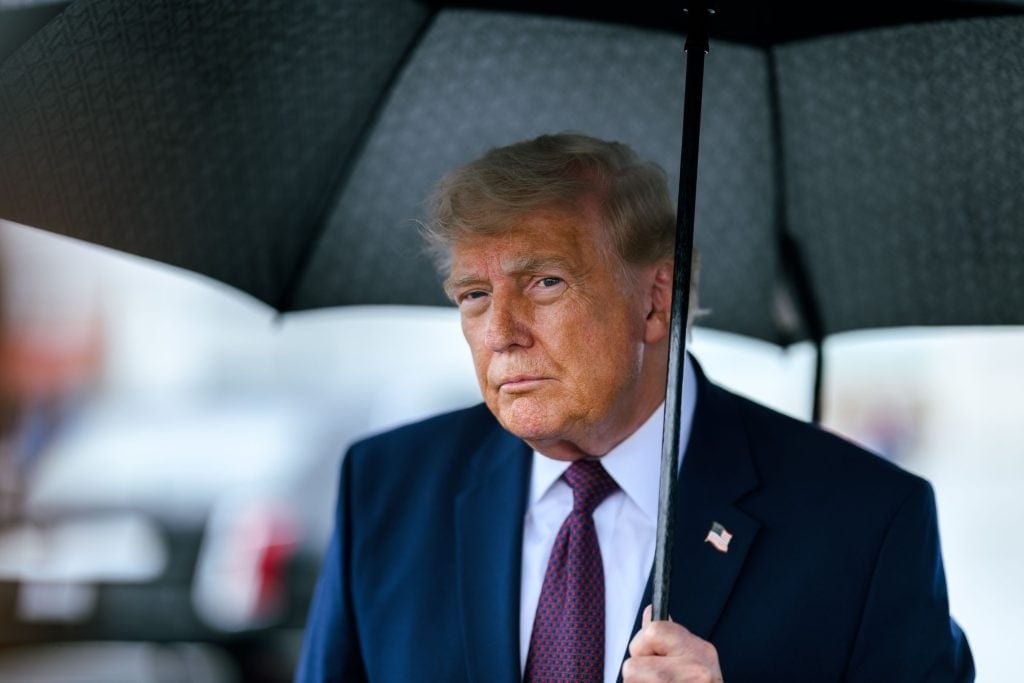 Donald Trump is holding an umbrella while speaking with the press.