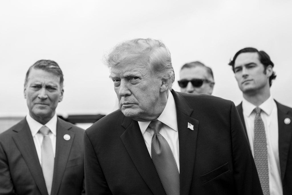 Government officials surround Donald Trump as he prepares to speak to the press.