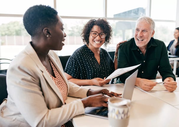 three people sitting at a table smiling and looking at paperwork.jpg