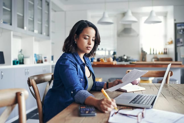 person holding document and writing note with laptop in front of them.jpg