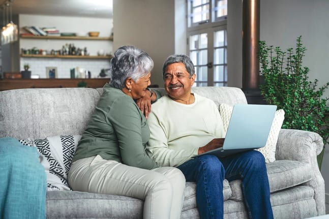 two older people sitting on a couch using a laptop and smiling.jpg