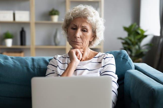 person with hand on chin looking at laptop SFkGg