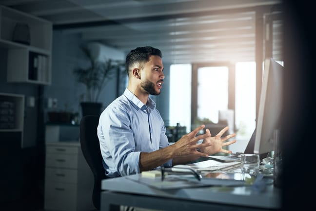 an angry person with hands outstretched looking at a computer monitor