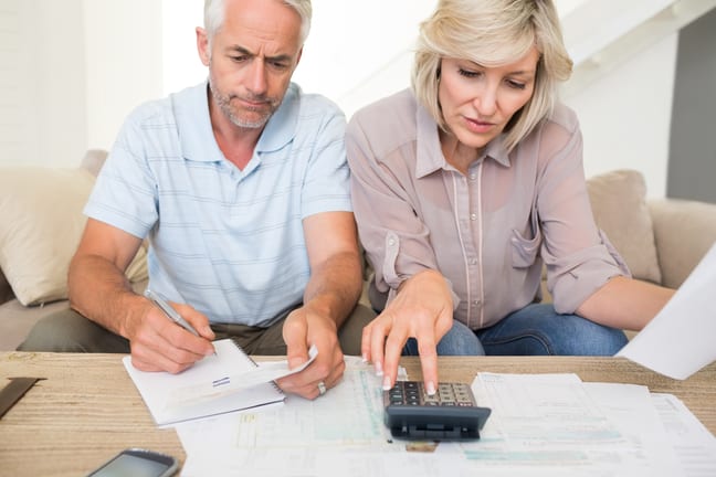 mature couple looking at documents and using calculator bills finances