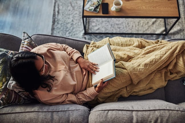 person on couch with blanket and book xRKWoBo.width .jpg