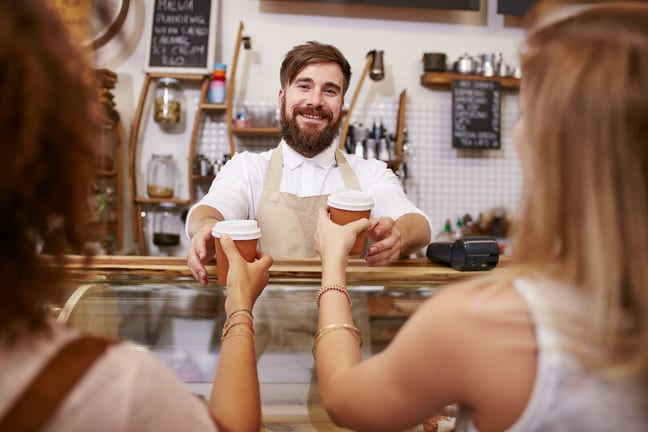 Smiling barista hands coffee to two women PAB.width .jpg
