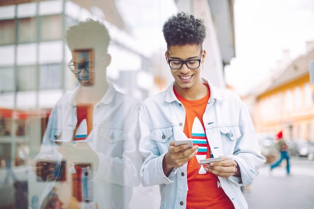 Teen boy using his phone and holding a credit.width .jpg