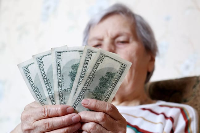elderly woman retirement social security holding one hundred dollar bills cash getty.jpg